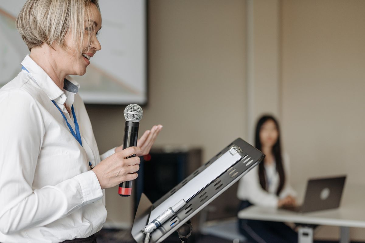Woman speaking into a microphone beside her presentation notes.